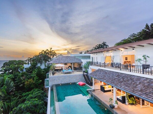 Una casa moderna con piscina, mobiliario exterior y vista al océano.