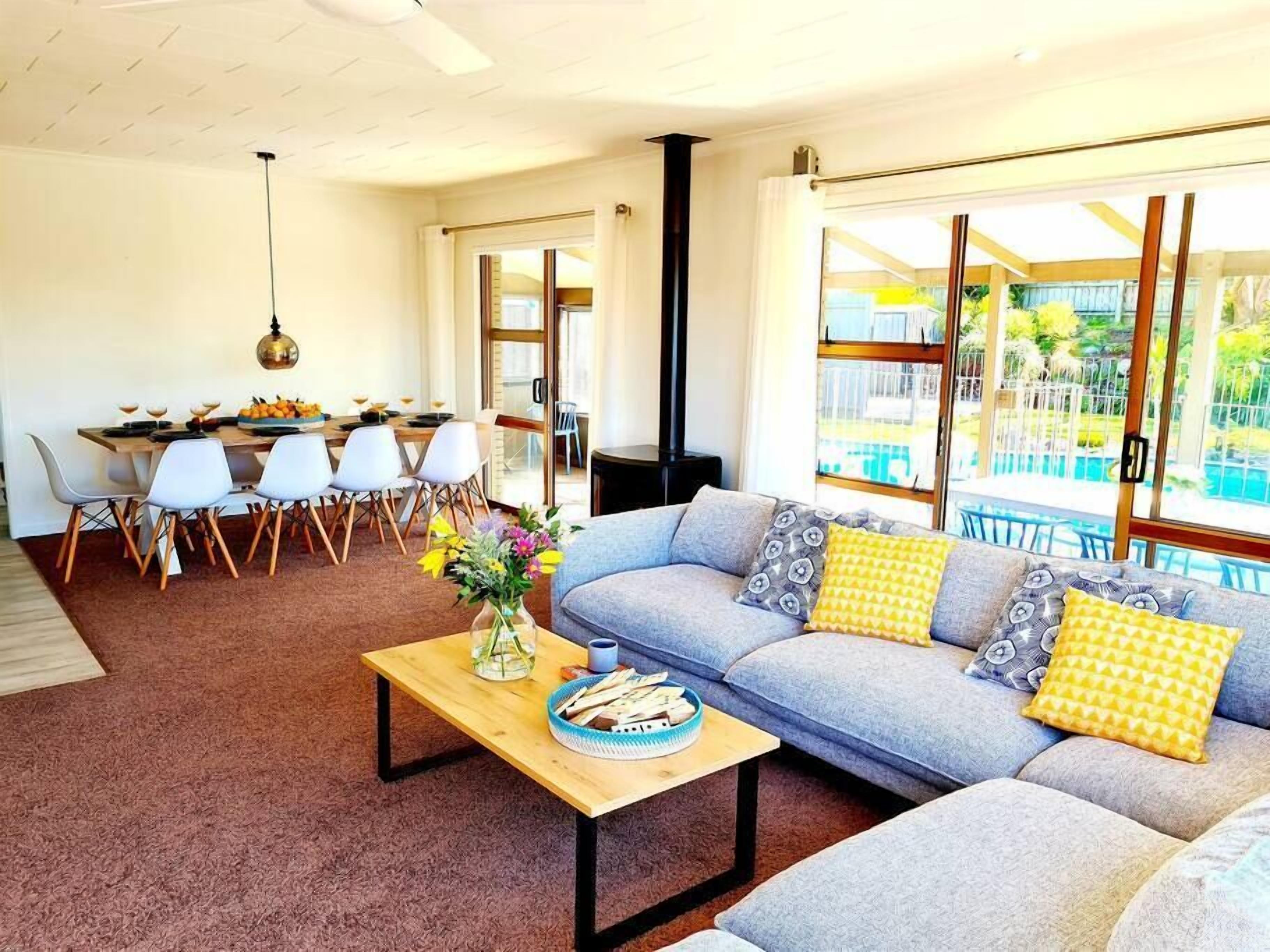A modern living room with a grey sofa, a wooden coffee table, and a dining area with a white table and chairs.