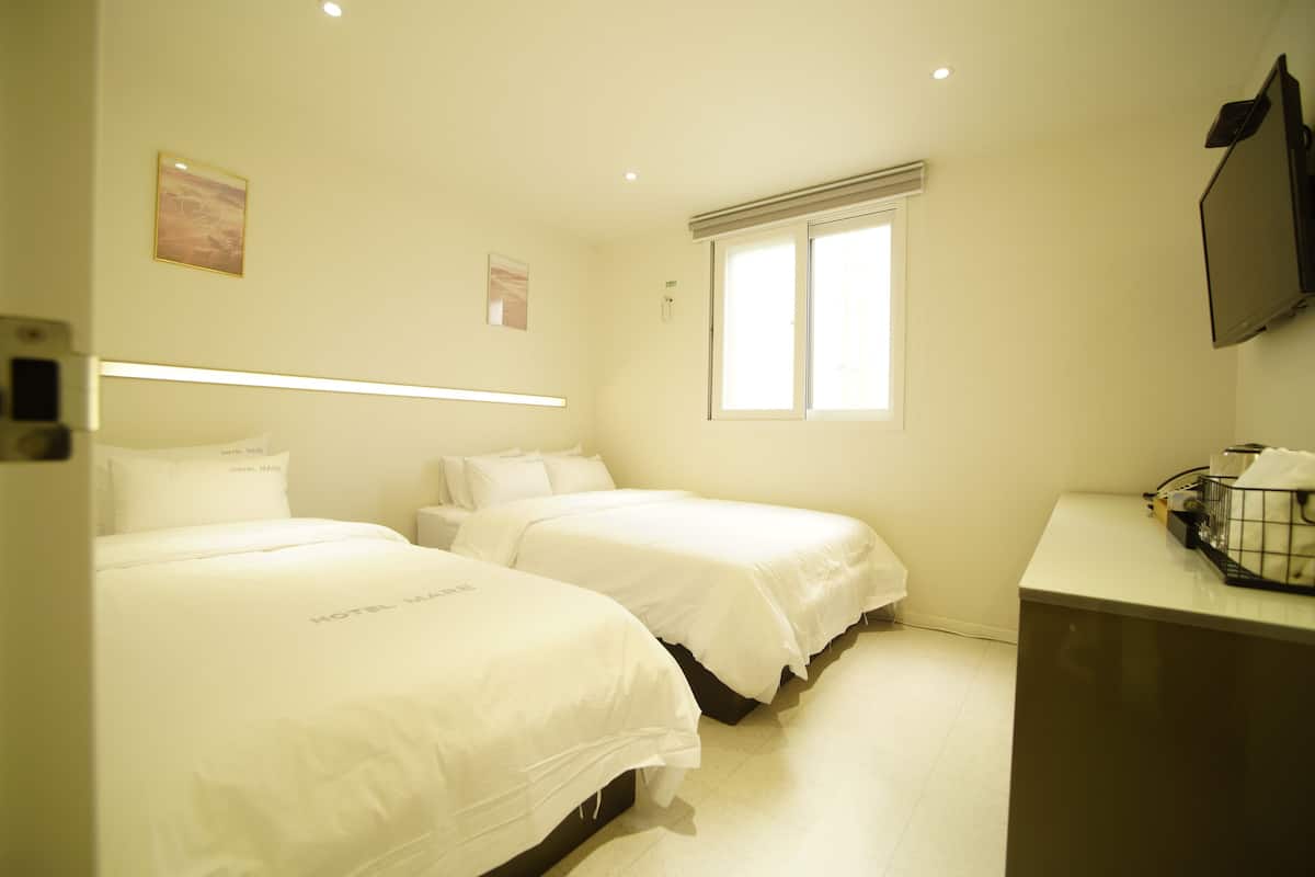 A hotel room with two beds, a bedside table, a TV, and a window.
