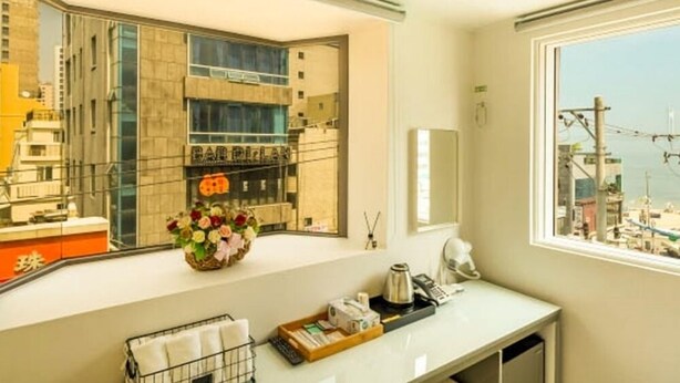 A modern bathroom with a large window, a sink, a mirror, and a vase with flowers. - Hotel Mare (Busan)