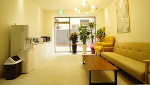 A reception area with a sofa, a coffee machine, a trash bin, and potted plants. - Hotel Mare (Busan)