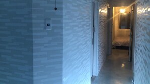 A narrow hallway with patterned walls and a door leading to a room with a bed and a nightstand. - Sapporo Princess Hotel - Hostel (Sapporo)