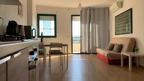 Una cocina moderna con estufa, microondas y comedor con sillas y mesa. Hay un sofá y una pequeña mesa con una planta.