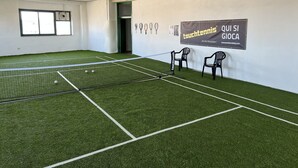 Una cancha de tenis con césped artificial, una red y dos sillas.