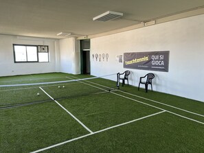 Una cancha de tenis con césped artificial, una red y dos sillas.