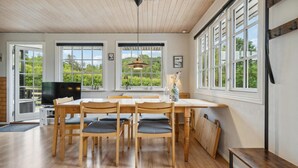A dining area with a wooden table and chairs, a television, and large windows with a view of greenery. - Cozy home in Tranekær with kitchen (Tranekær)