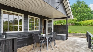 A wooden deck with a table and chairs, a grill, and a view of a green landscape. - Cozy home in Tranekær with kitchen (Tranekær)