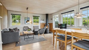 A spacious living area with a fireplace, comfortable seating, and large windows offering a view of the outdoors. - Cozy home in Tranekær with kitchen (Tranekær)