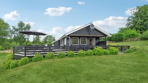 A modern cabin with a covered porch, surrounded by a wooden deck and lush greenery. - Cozy home in Tranekær with kitchen (Tranekær)