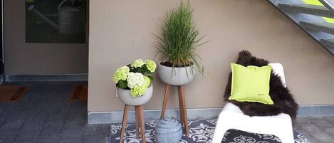 A staircase with a metal handrail, a bright yellow wall, a welcome mat, two potted plants, a patterned rug, and a white chair with a green pillow.