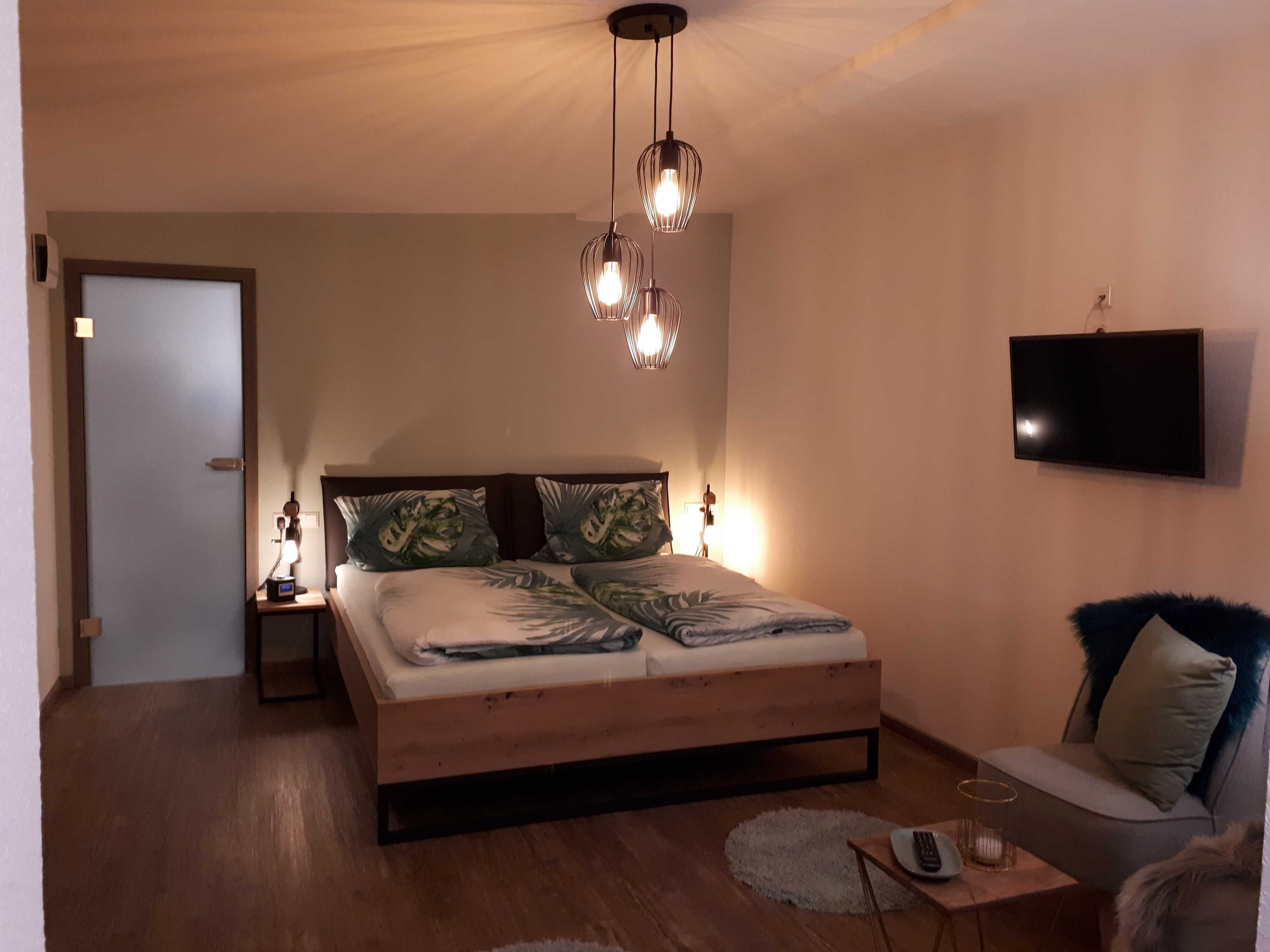 A bedroom with a wooden bed, a TV mounted on the wall, and a ceiling light fixture.
