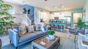 A modern living room with a gray sofa, a coffee table with a plant, and a staircase leading to the kitchen.