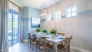A dining area with a large table, chairs, potted plants, and a chandelier.