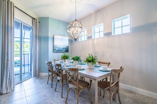 A dining area with a large table, chairs, potted plants, and a chandelier.