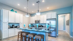 A modern kitchen with white cabinets, a central island with bar stools, stainless steel appliances, and pendant lighting.