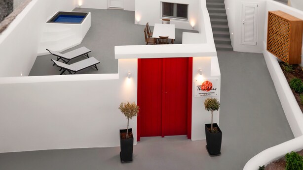 A modern white building with a red door, a staircase, and a pool area. - Thallos Cave House and Apartments (Santorini)