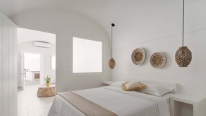 A modern bedroom with a large bed, a bedside table, and a window. - Thallos Cave House and Apartments (Santorini)