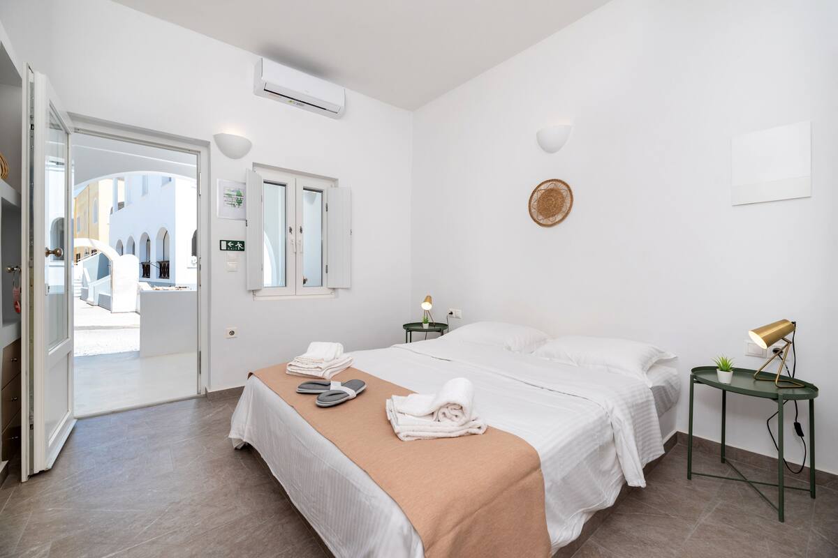 Une chambre d’hôtel avec un lit, des tables de chevet, une petite table avec une lampe et une vue sur la rue.