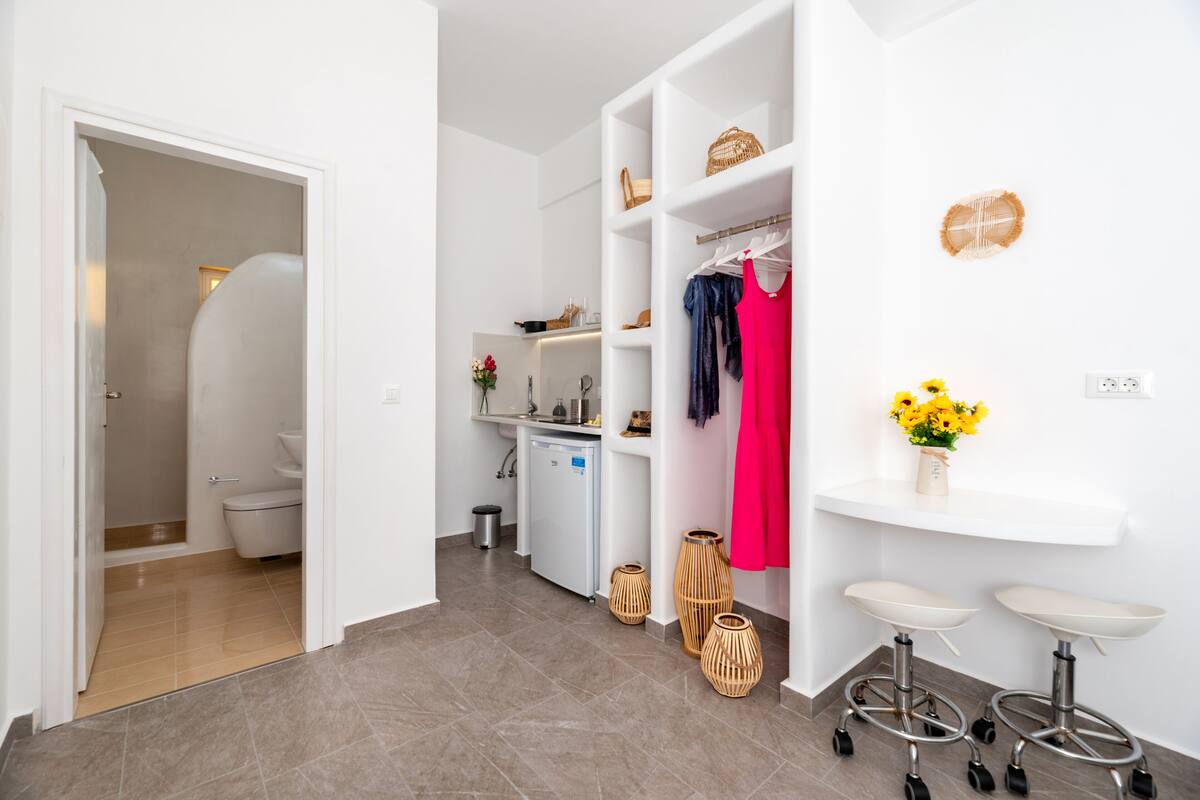 Une salle de bain moderne avec douche, toilettes et lavabo. Il y a également une petite kitchenette équipée d’un réfrigérateur et d’une machine à café.