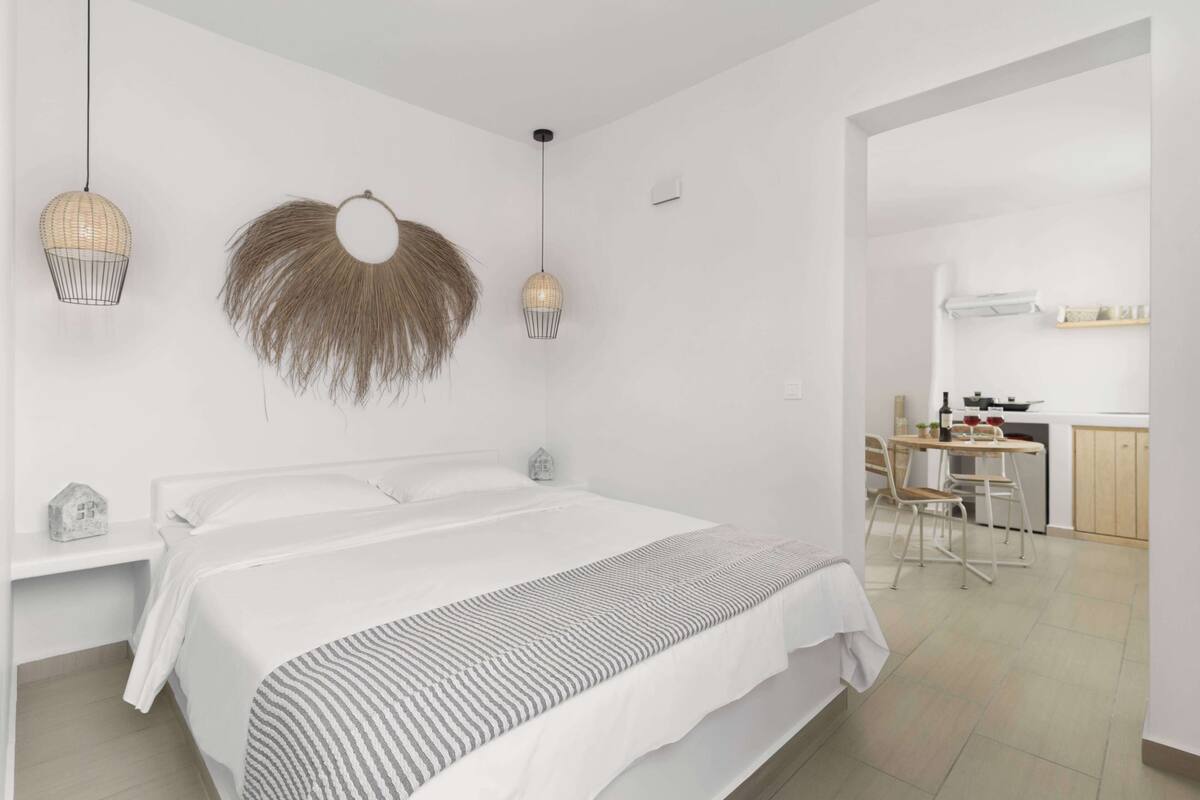 Une chambre à coucher moderne avec un grand lit, des tables de chevet et un coin cuisine à l’arrière-plan.