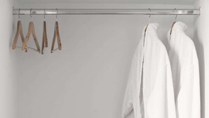 A bathroom with a wooden vanity, two wicker baskets, and two white bathrobes hanging on a metal rod. - Thallos Cave House and Apartments (Santorini)