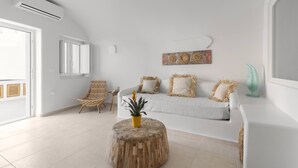 A modern living room with a white sofa, a wooden ottoman, and decorative pillows. - Thallos Cave House and Apartments (Santorini)
