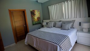 Une chambre à coucher avec un lit, des lampes de chevet, une porte en bois, un tableau et une fenêtre avec des rideaux.