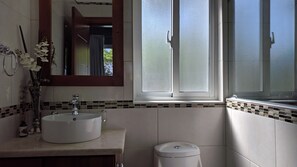 Une salle de bain avec un lavabo blanc, un miroir, une fenêtre et des toilettes.