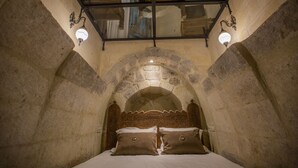 A stone-walled room with a bed, a glass ceiling, and two wall-mounted lights. - Sinasos Star Hotel Cappadocia (Ürgüp)