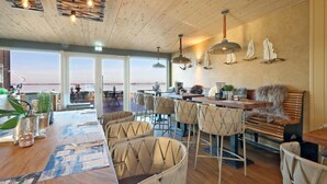 Een ruime eethoek met uitzicht op het water, een houten plafond en moderne hanglampen.