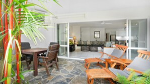 A spacious patio with a stone floor, wooden furniture, and a view into the living area.