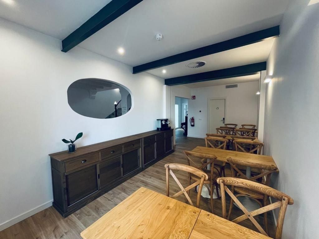 Un comedor con mesas y sillas de madera, un mueble de madera oscura y un espejo ovalado grande en la pared.