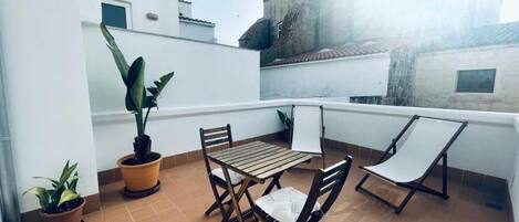 Una terraza con mesa y sillas, plantas en macetas y vistas a edificios.