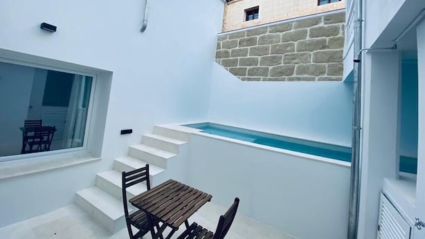 Un espacio exterior moderno con piscina, una mesa de madera y un muro de piedra.