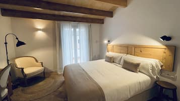 A bedroom with a wooden headboard, a bed with white linens, a chair, a floor lamp, and a small stool.