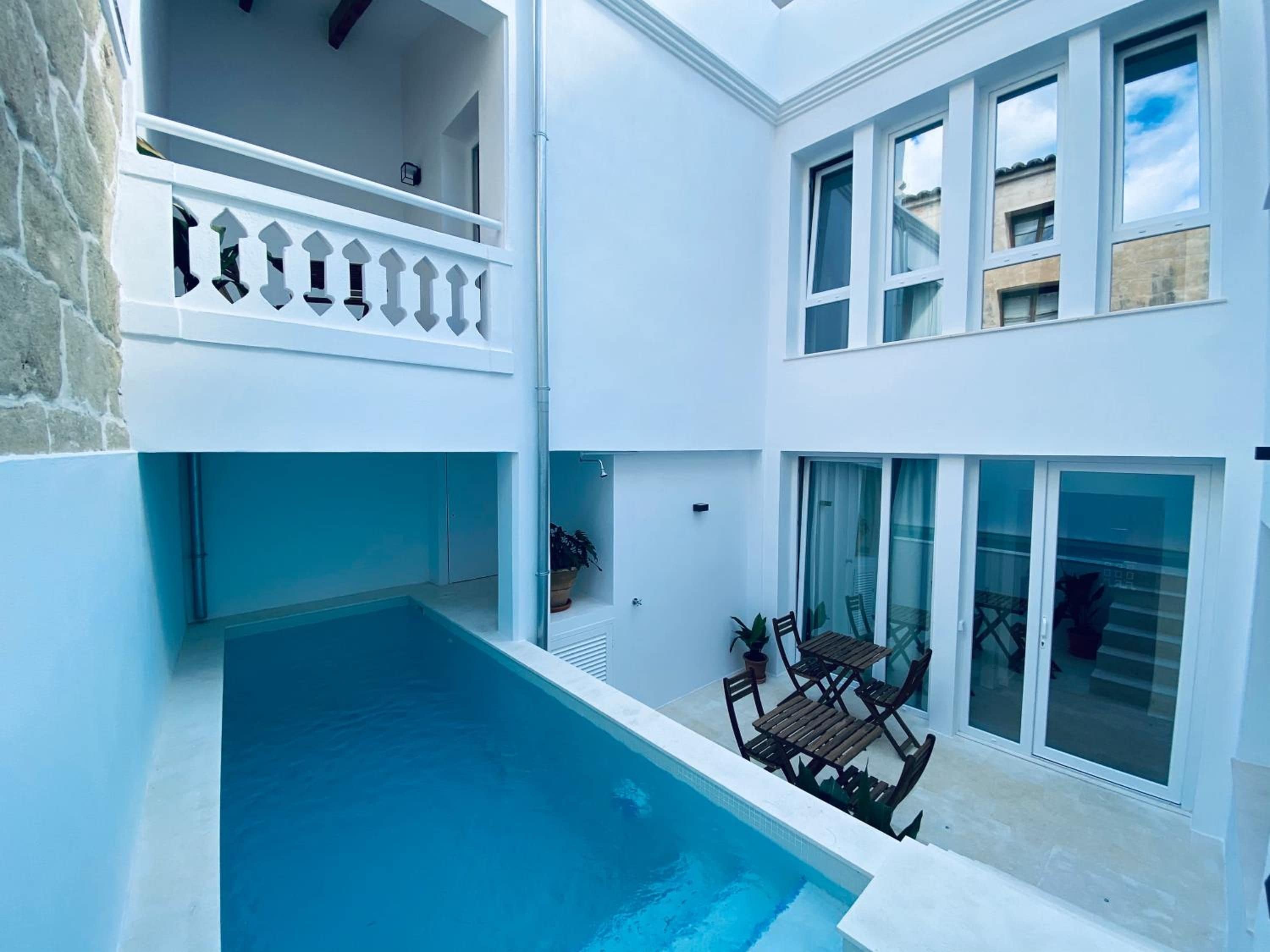 Un edificio de dos pisos con piscina en la planta baja, un balcón con barandilla blanca y ventanas amplias en el nivel superior.