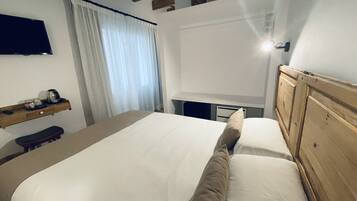 Un dormitorio con una cama, cabecera de madera, mesita de noche, estante con objetos y una ventana con cortinas.