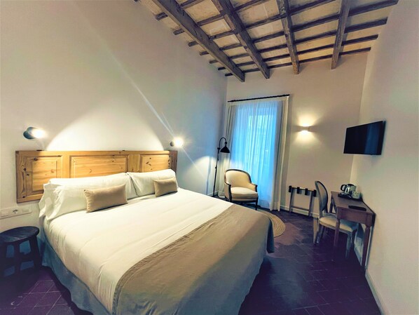 A bedroom with a wooden headboard, a bed with white bedding, a chair, a desk with a flat-screen TV, and a window with curtains. - Hotel Casa Miranda - Adults Only (Mahón)