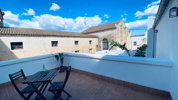 A terrace with a table and chairs, potted plants, and a view of buildings with tiled roofs.