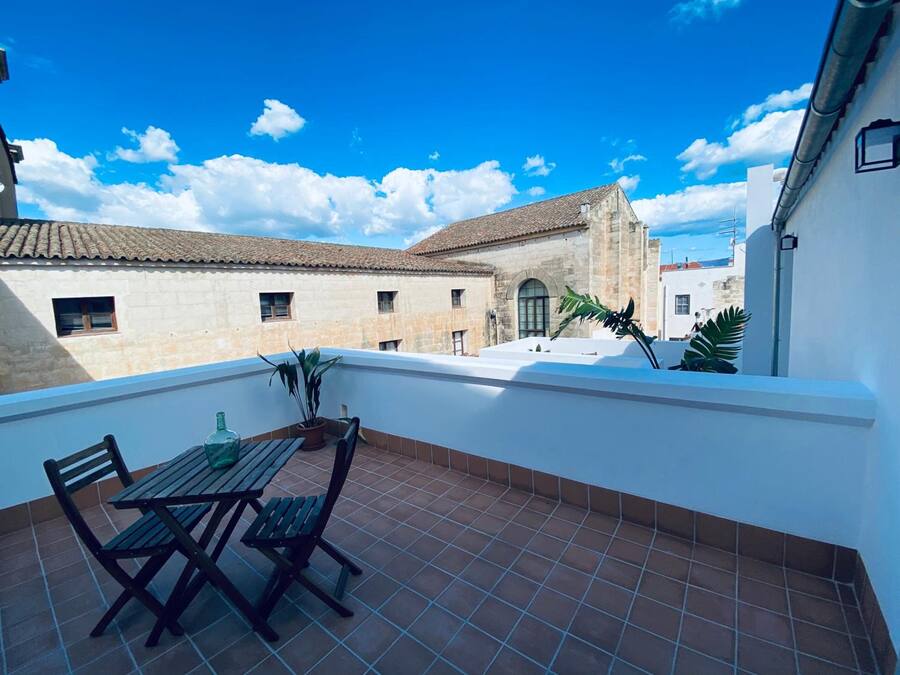 Una terraza con una mesa y sillas, plantas en macetas y vistas de edificios con tejados de tejas.