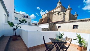 Terraza en la azotea con mesa y sillas, plantas en macetas y vista a un edificio histórico.