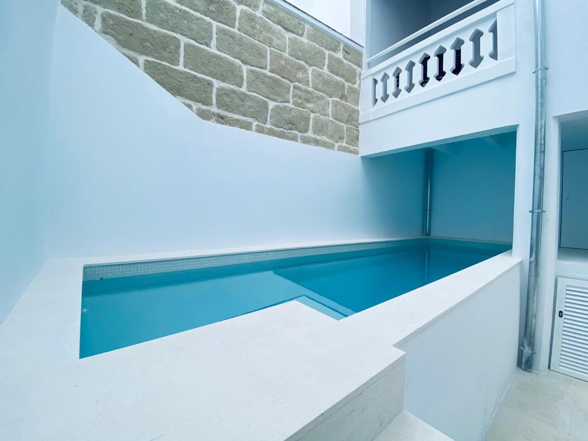 Una piscina interna moderna con un elemento d'acqua blu cristallina, una parete in mattoni e un balcone bianco con ringhiera.