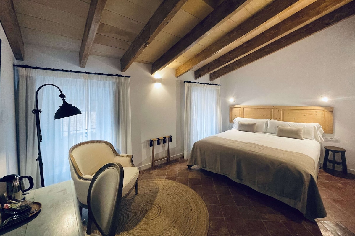 Quarto com cama, uma cadeira, escrivaninha com luminária e cafeteira.
