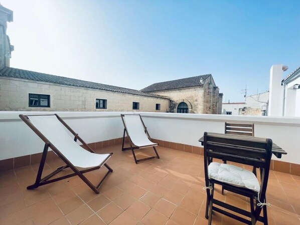 A terrace with two lounge chairs and a table, overlooking a historic building with a tiled roof.