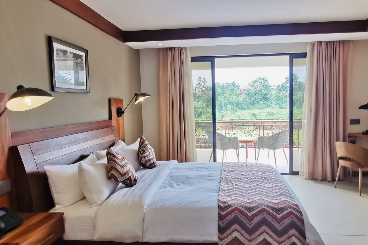 A hotel room with a bed, bedside tables, a desk, a chair, and a balcony with a view.
