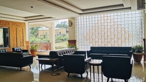 A spacious lobby with a seating area, a reception desk, and large windows offering a view of the outdoors. - Kampala Nile Resort (Seeta)