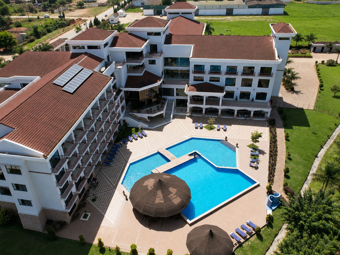 A multi-story hotel with a central swimming pool, outdoor seating, and a well-maintained lawn.