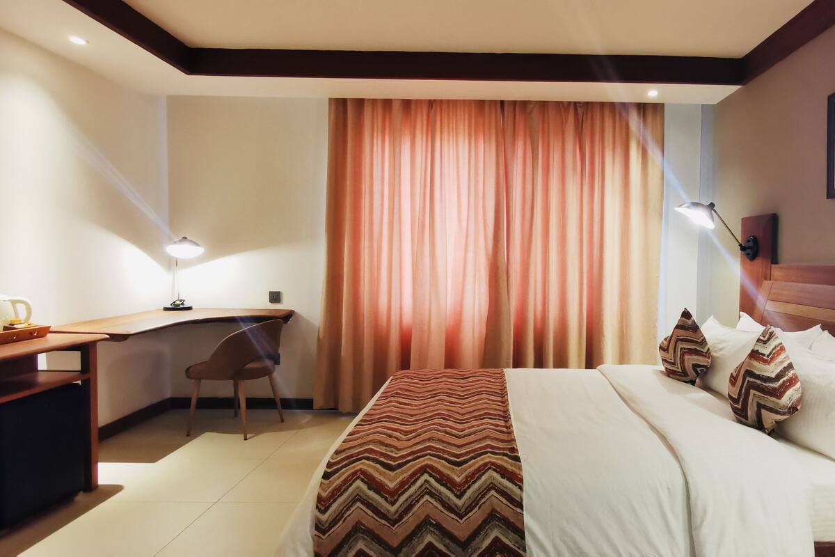 A hotel room with a bed, desk, chair, and a telephone.
