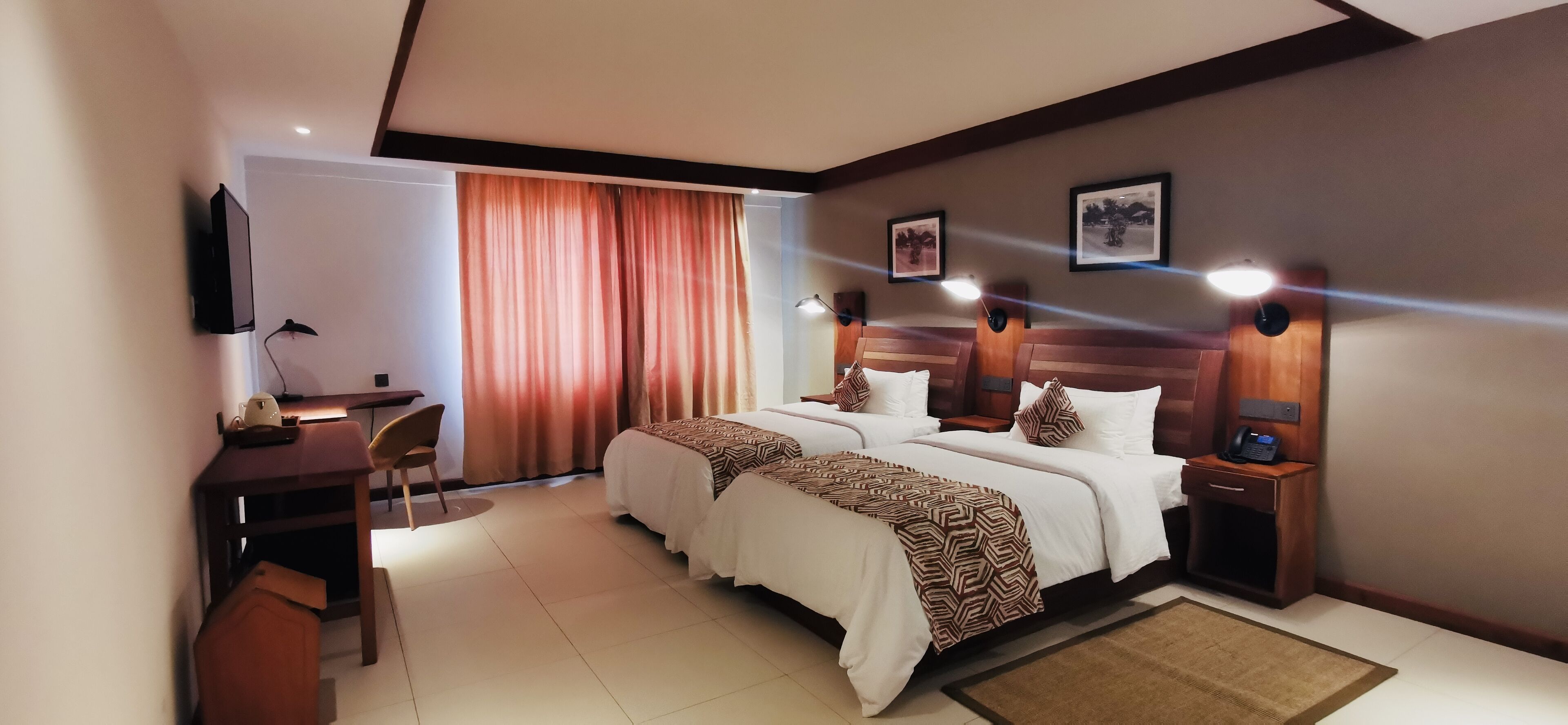 A hotel room with a bed, bedside tables, a desk, a chair, and a TV.