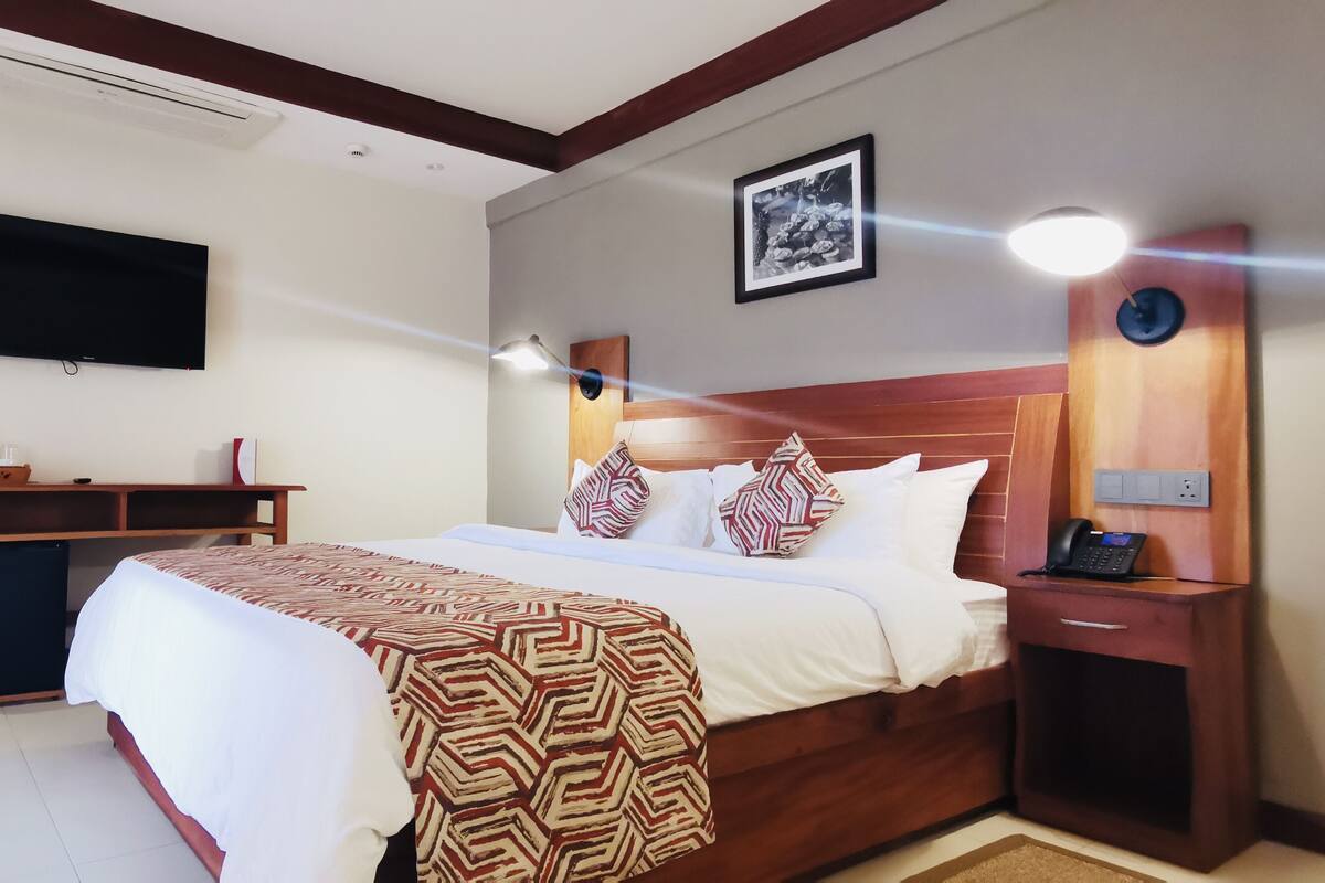A hotel room with a bed, bedside table, desk, and a flat-screen TV mounted on the wall.